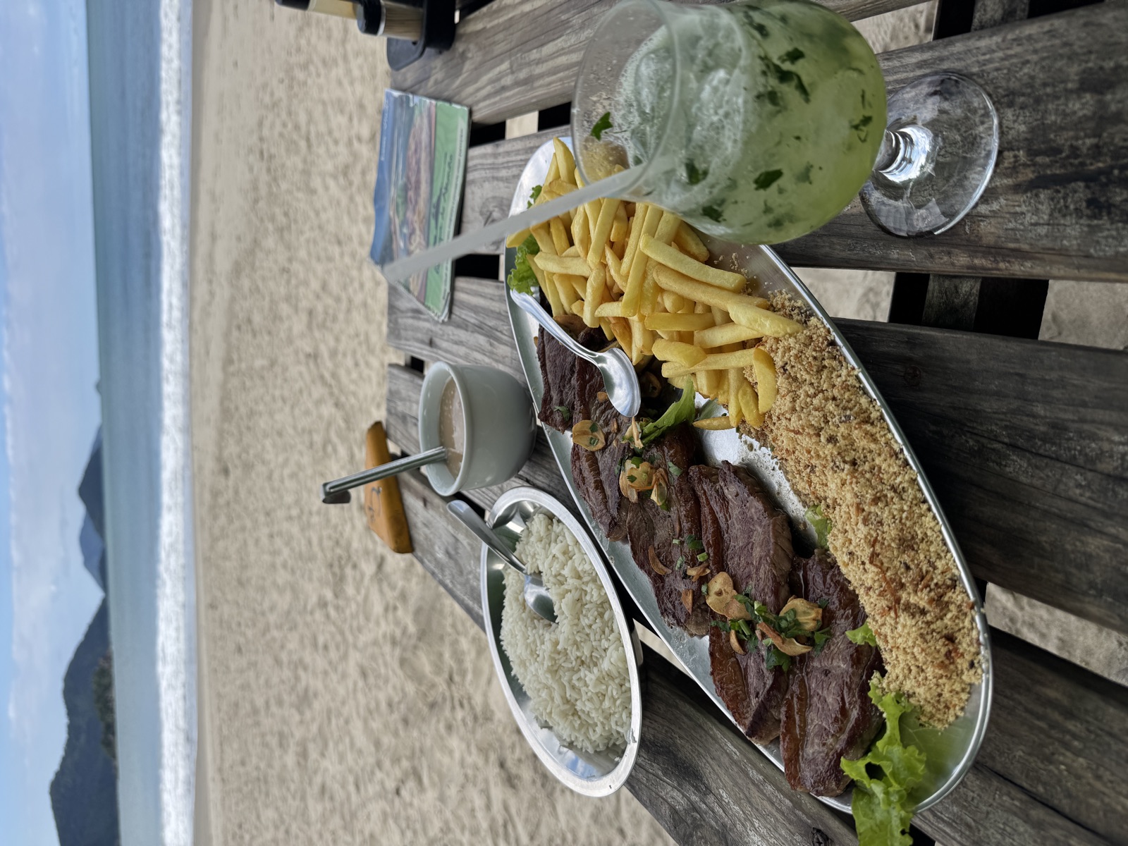 Gegrilltes Fleisch, Reis, Pommes und Caipirinha am Strandtisch